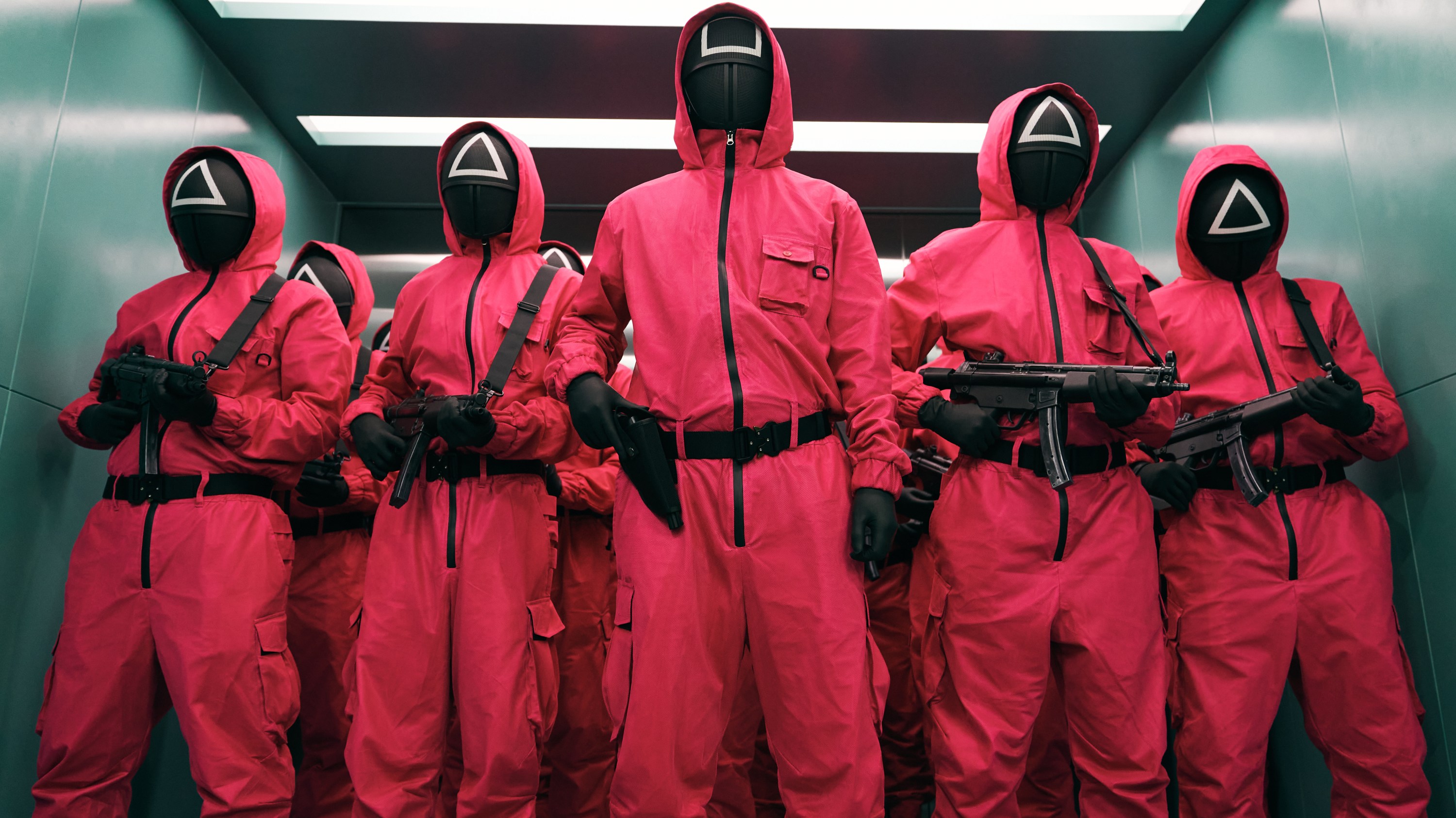 A group of people in red jumpsuits with hoods and masks featuring geometric shapes; still from 'Squid Game'