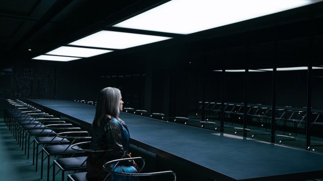 Patricia Arquette in 'Severance' Season 2, shown sitting alone at a long, black conference table with black chairs in a black room at night