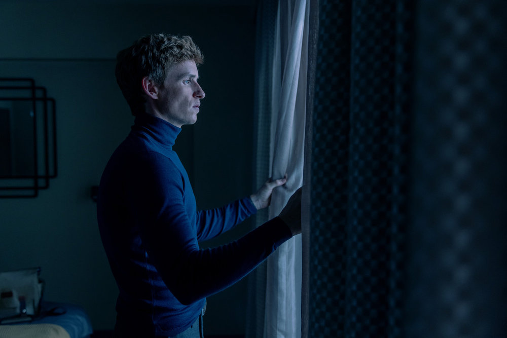 THE DAY OF THE JACKAL Episode 10 stars Eddie Redmayne as the Jackal, shown here looking out a window in a blue turtleneck